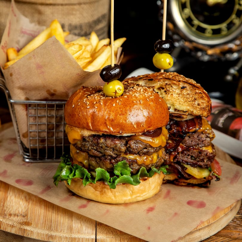 Two juicy double cheeseburgers with olives on top, served with a side of golden fries.