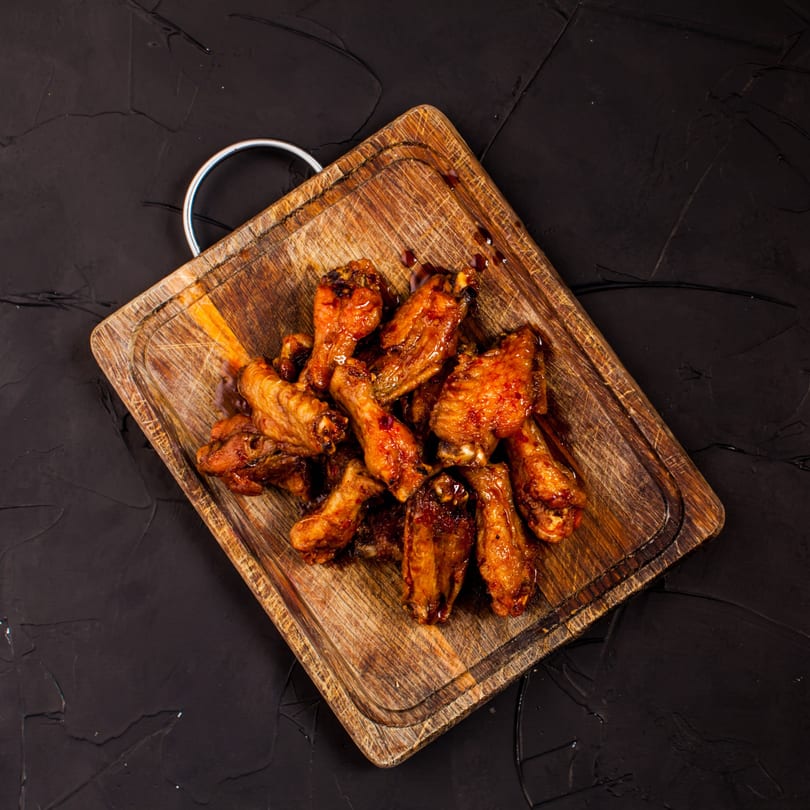 Wacky Zaki's chicken wings, glazed with sauce, served on a rustic wooden cutting board.