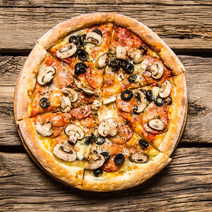 Wacky Zaki's pizza with mushrooms, olives, and pepperoni on a rustic wooden table.